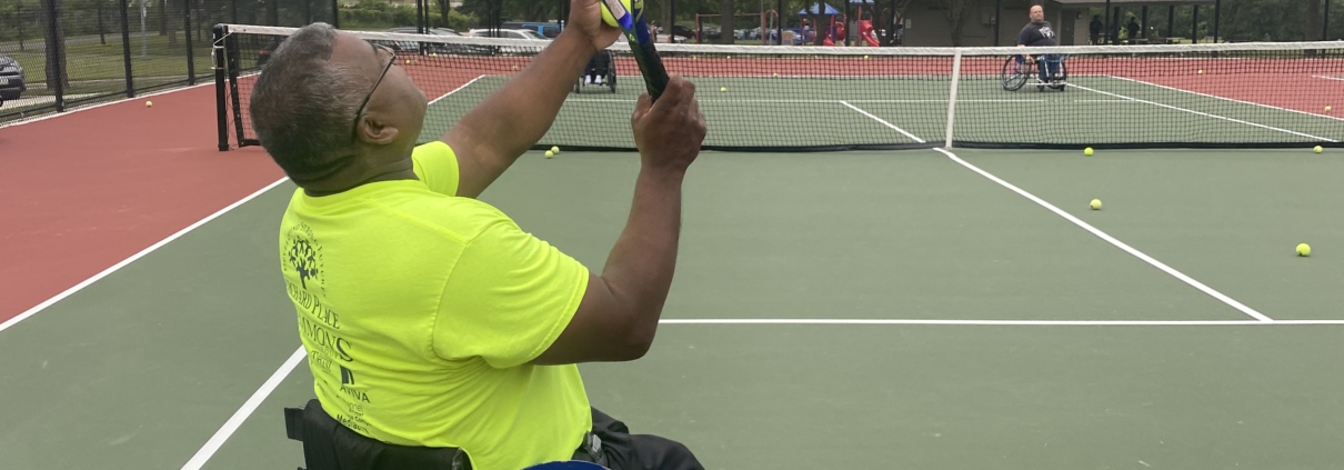 Mike holding his racquet and looking up as he tosses a tennis ball in the air to serve.