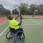 Mike holding his racquet and looking up as he tosses a tennis ball in the air to serve.