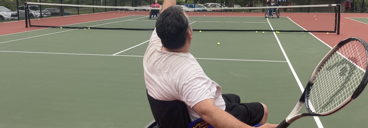 Joel is tossing up a tennis ball and getting ready to serve it over the net.