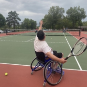 Joel is tossing up a tennis ball and getting ready to serve it over the net.