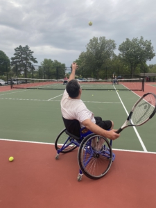 Joel is tossing up a tennis ball and getting ready to serve it over the net.