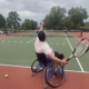 Joel is tossing up a tennis ball and getting ready to serve it over the net.