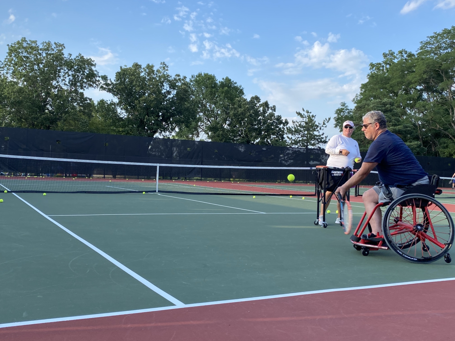 A man in a sport wheelchair, reaching to hit a tennis ball with his racquet
