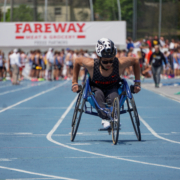 Josh pushing his racing wheelchair over the finish line on the blue track at Drake University