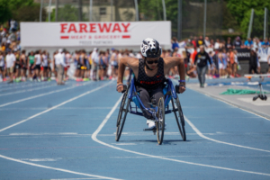 Josh pushing his racing wheelchair over the finish line on the blue track at Drake University