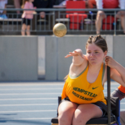 Ally sitting in a shot put chair, throwing the implement in her yellow team track jersey.