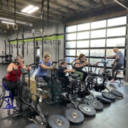 Four women working out next to each other. They are all seated and using a stationary bike with their arms.