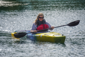 A woman sitting in a kayak with outriggers that help with balance. She is wearing a lifejacket and smiling at the camera.